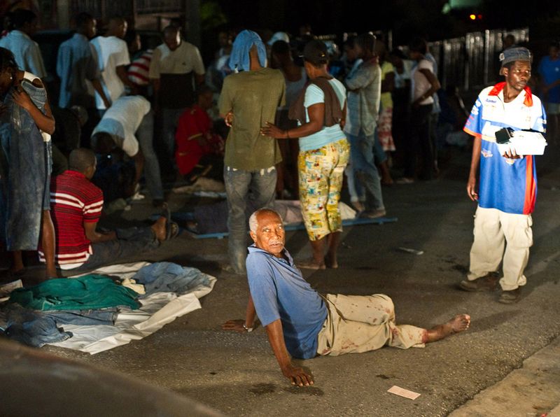 Мужчина с двумя поломанными ногами сидит на улице среди других раненых после землетрясения 13 января в Порт-о-Пренс