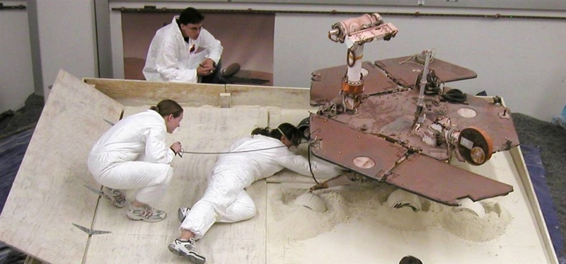 Члены команды Марс-ровера Скотт Максвелл, Паулин Хван и Ким Лихтенберг готовят тест-ровер для сессии 9 июля, целью которой является найти наилучший способ пересыпать мягкий грунт в специально собранный «мусорный контейнер» в лаборатории NASA. Результаты этого теста помогут инженерам создать стратегию для ровера NASA, который попал в затруднительную ситуацию на Марсе. (NASA/JPL-Caltech)