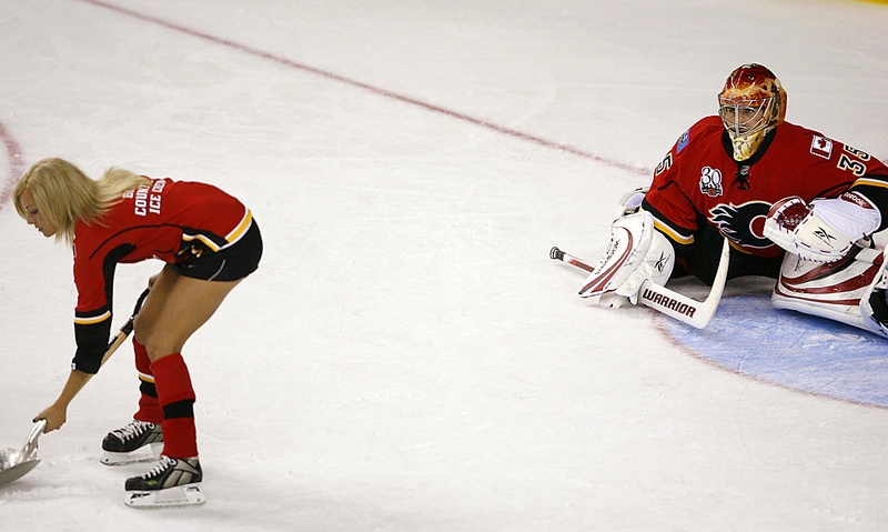 Вратарь команды «Calgary Flames» Леланд Ирвинг наблюдает за тем как девушка из персонала команды убирает снег со льда в перерыве после второго периода предсезонки НХЛ против «Edmonton Oilers» в Калгари, Альберта, Канада.