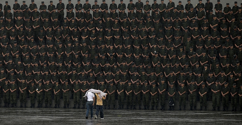 Двое идут под дождем в сторону группы солдат во время военной церемонии в Мехико. Сотни солдат маршировали перед президентом Фелипе Кальдероном в рамках церемонии вручения дипломов кадетам.