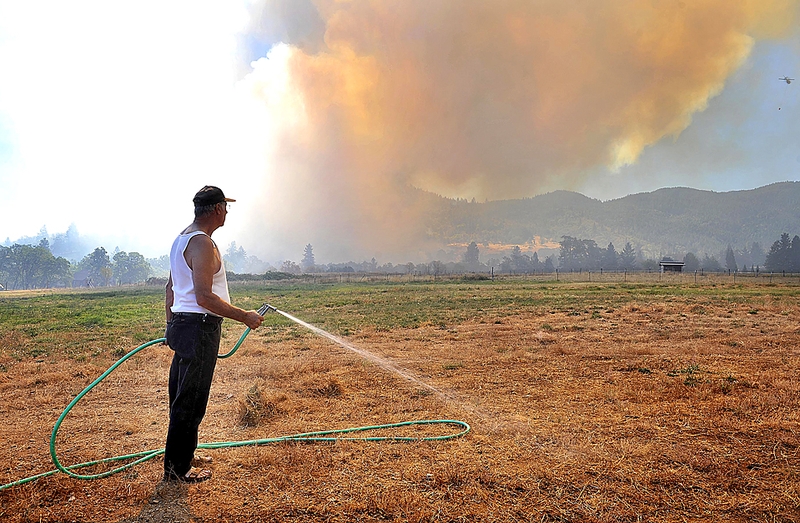 Барри Коверт обливает поле, в то время как пожар подходит с юга к Эшланду, штат Орегон. Местные жители, которые были эвакуированы из близлежащего Медфорда, начали снова возвращаться по домам после того, как увлекаемый ветром огонь прошел мимо. К вечеру понедельника огонь испепелил около 600 акров земли.