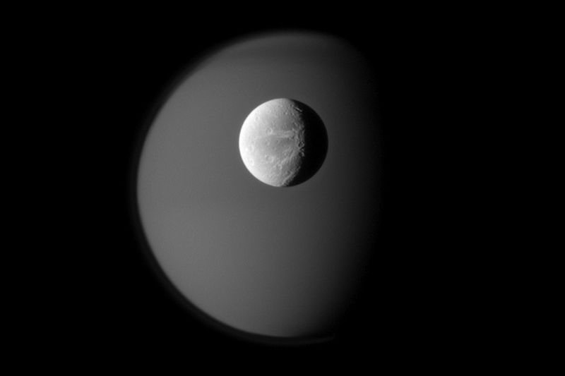 Поверхность спутника Сатурна Дионы на фоне туманного призрачного Титана 10 апреля. Снимок был сделан аппаратом «Кассини» на расстоянии приблизительно 1,8 миллионов км от Дионы и 2,? Миллионов километров от Титана. (NASA/JPL/Space Science Institute)