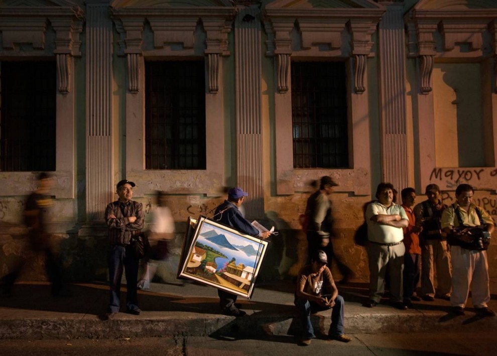 Торговец картинами проходит мимо участников акции протеста, которые собрались у здания конгресса Гватемалы. 