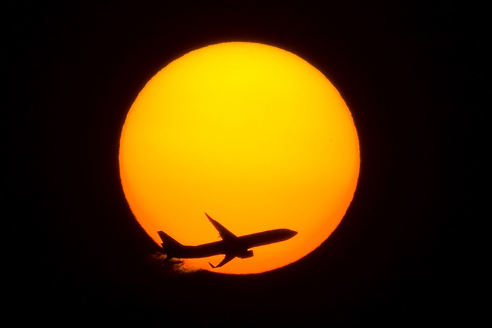 Пассажирский самолет пролетает на фоне заходящего солнца в Шанхае