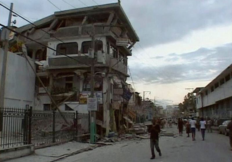 Люди идут по улице мимо разрушеных от землетрясения домов в Порт-о-Пренс 12 января.