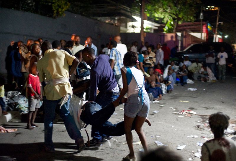 Оставшиеся без крова люди выносят раненого из больницы, после начала третьего толчка 13 января в Порт-о-Пренс.
