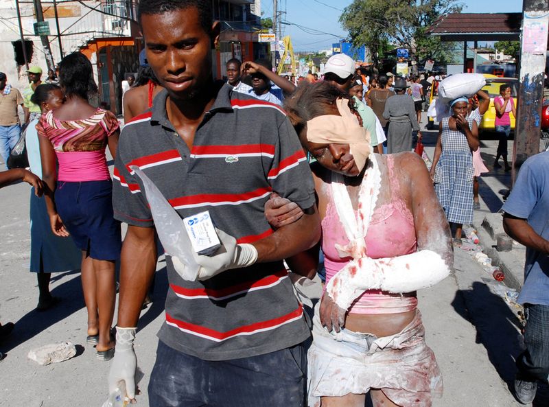 Раненую девушку ведут по одной из улиц гаитянской столицы.