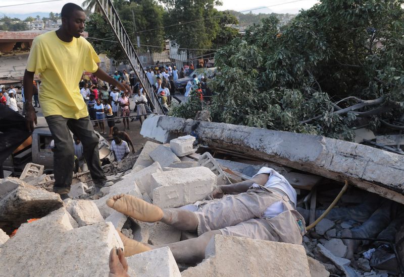 Молодой человек подходит к трупам, лежащим в обломках здания у дороги Делмас в гаитянской столице. 