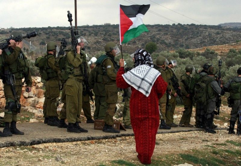 2. Израильские солдаты, мимо которых проходит палестинская женщина с национальным флагом, во время проведения акции протеста в деревне Билин против разделительного барьера, возле города Рамаллах, Западный берег реки Иордан, 31 декабря 2010 года. Лидеры Палестины заявили, что они обратятся в ООН, чтоб территорию их государства признали в рамках границ, которые были в 1967 году, невзирая на все территориальные притязания Израиля.