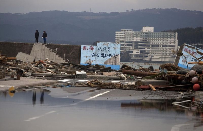 Два человека стоят возле разрушенного волнолома (справа) в поселке Минамисанрику, северо-восточная Япония. Мэр поселка, Джин Сато, сказал, что не знает, какие меры должны быть предприняты для защиты населения от цунами в будущем. «Что мы можем сделать?» -задает он вопрос – «Построить волнолом высотой 25 метров?»