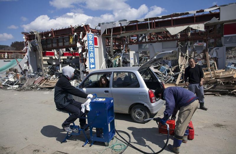 Люди обходятся насосом с велосипедным приводом для заправки автомобилей на месте бывшей заправки в разрушенном землетрясением и цунами поселке Минамисанрику, северо-восточная Япония.