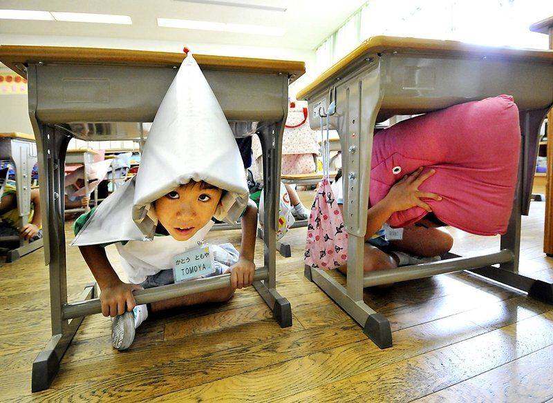 Ученики начальной школы в огнезащитных капюшонах прячутся под партами во время обучения поведению при землетрясениях, которое проводилось по всей стране в Токио