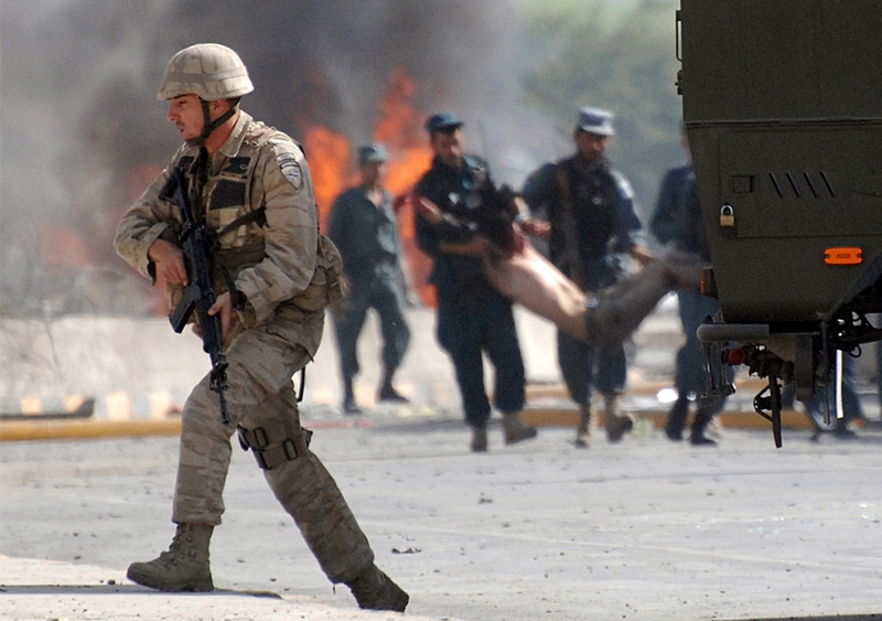 Афганские полицейские (на заднем фоне) помогают раненому на месте взрыва бомбы у главных ворот военного аэропорта НАТО в Кабуле 8 сентября 2009 года. Террорист-смертник взорвал автомобиль у военного аэропорта Кабула 8 сентября, убив двух афганских граждан и ранив 10 человек, включая четырех иностранных солдат.