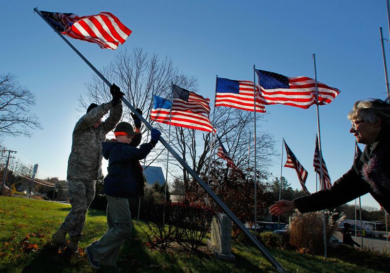 Старший сержант Билл Росс – 35-летний ветеран ВВС – и 12-летний бойскаут Лайям Галлахер поднимают один из 50 br флагов в память о местных ветеранах в Фрипорте, штат Мэн. Гли Робинсон Росс (слева) помогает им.