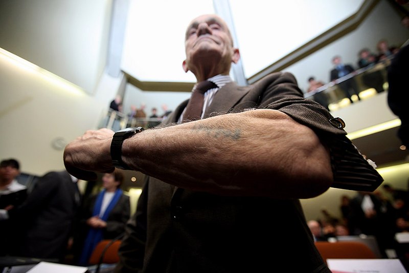 Роберт Коэн показывает татуировку, которую ему сделали в концлагере Аушвиц-Биркенау. Снимок сделан в зале суда в Мюнхене во время судебного разбирательства над Джоном Демьянюком, которого обвиняют в убийстве 27900 евреев. Демьянюк был депортирован из США в мае. Ему грозит до 15 лет тюремного заключения